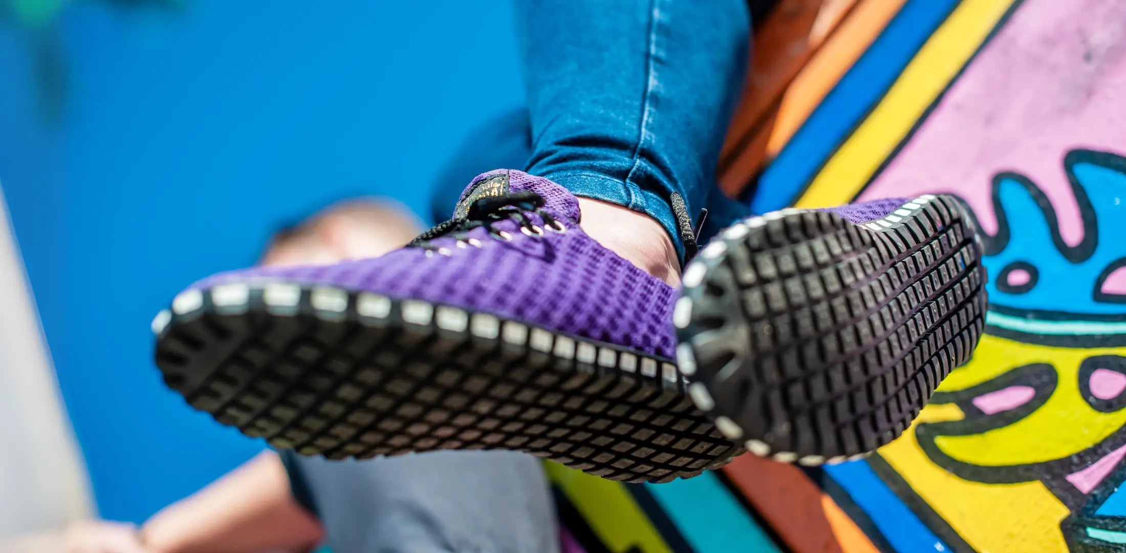 Close-up of a person's feet in sporty purple shoes against a colorful graffiti background.